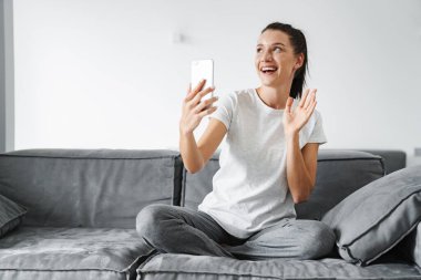 Avrupa 'dan gülümseyen bir kadın cep telefonuyla el kol hareketi yapıyor ve selfie çekiyor.