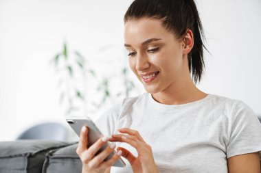 Avrupa 'dan gülümseyen bir kadın evdeki koltukta otururken cep telefonu kullanıyor.
