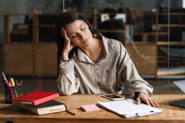 Genç, yorgun, sıradan esmer, beyaz bir kadın ofis masasında uyuyor.