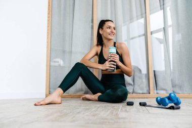 Beyaz esmer kadın evde çalışırken gülümsüyor ve su içiyor.