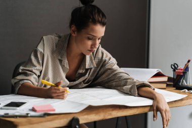 Genç esmer kadın ofiste otururken çizimlerle çalışıyor.