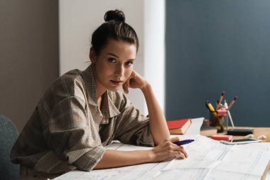 Genç esmer kadın ofiste otururken çizimlerle çalışıyor.