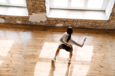 Genç esmer beyaz kadın stüdyo manzarasında çağdaş dans ediyor.