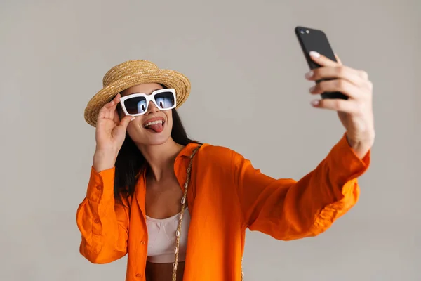 Młoda Brunetka Kapeluszu Okularach Przeciwsłonecznych Robi Selfie Komórce Odizolowany Szarym — Zdjęcie stockowe