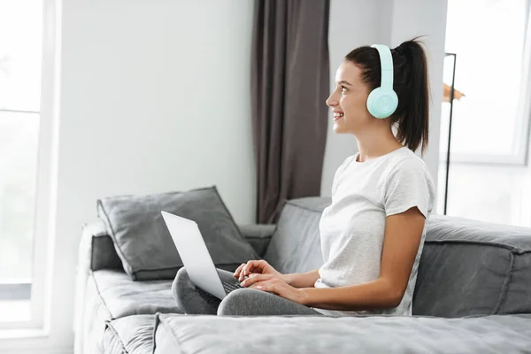 Europeo Donna Sorridente Utilizzando Cuffie Laptop Mentre Seduto Sul Divano — Foto Stock