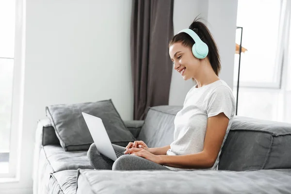 Mujer Sonriente Europea Usando Auriculares Portátil Mientras Está Sentada Sofá —  Fotos de Stock