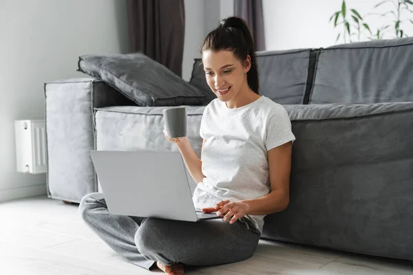 Sorrindo Mulher Bebendo Café Usando Laptop Enquanto Sentado Chão Casa — Fotografia de Stock