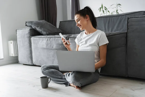 Lächelnde Frau Benutzt Handy Und Laptop Während Sie Hause Auf — Stockfoto