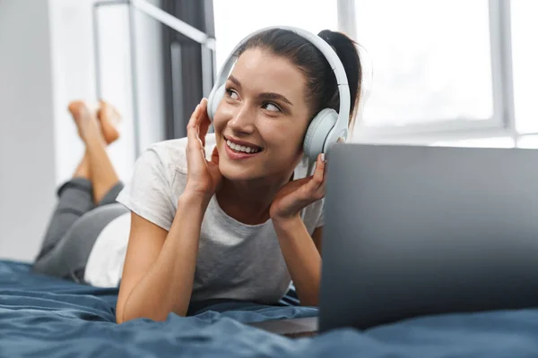 Europeo Donna Sorridente Cuffia Utilizzando Computer Portatile Mentre Sdraiato Sul — Foto Stock