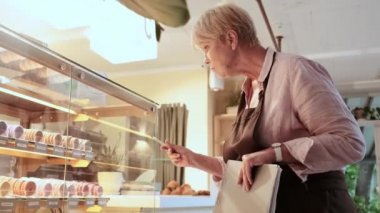 Yoğunlaşmış bir kadın kafe çalışanı kafedeki bir dükkanın camını pastalarla kontrol ediyor.