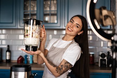 Mutfakta smoothie hazırlarken cep telefonuyla selfie çeken beyaz bir kadın.