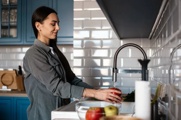 快乐的中年黑发女人在厨房的水槽里洗水果 — 图库照片