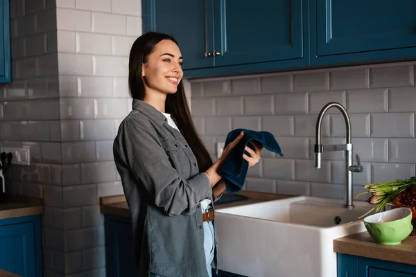 快乐的中年黑发女人站在厨房的水槽边用毛巾洗手 — 图库照片