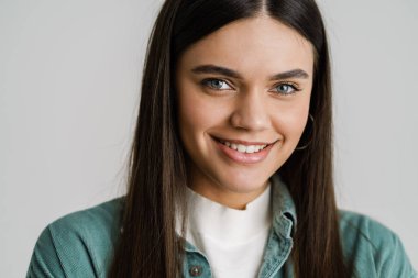 Genç esmer kadın gülümsüyor ve beyaz arka planda izole edilmiş kameraya bakıyor.