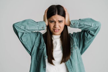 Genç hoşnutsuz bir kadın beyaz arka planda başını tutarken kameraya bakıyor.