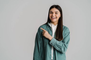 Genç esmer kadın gülümsüyor ve beyaz arka planda izole edilmiş bir şekilde işaret ediyor.
