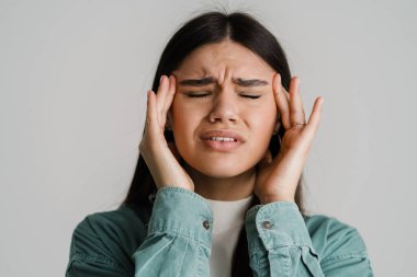 Baş ağrısı olan, şakaklarını ovuşturan, beyaz arka planda soyutlanmış genç mutsuz bir kadın.