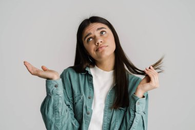 Kafası karışmış genç bir kadın, beyaz arkaplan üzerinde saçının bir tutamını ve boşluğunu tutuyor.