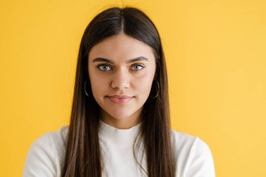 Genç esmer kadın poz veriyor ve sarı arka planda izole edilmiş kameraya bakıyor.