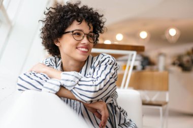 Kafedeki kanepede otururken gülümseyen gözlüklü güzel mutlu kadın.