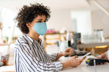 Kafede faturayı öderken cep telefonu kullanan kıvırcık yüzlü kadın.