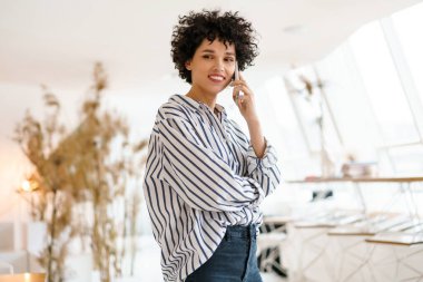 Güzel kıvırcık mutlu kadın cep telefonuyla konuşurken gülümsüyor.