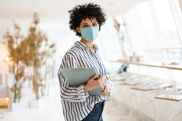 Beautiful Curly Nice Woman Face Mask Holding Clipboard While Standing — Stock Photo, Image