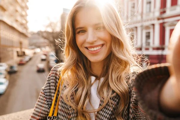 Sorrindo Jovem Loira Tomando Uma Selfie Enquanto Caminha Uma Rua — Fotografia de Stock