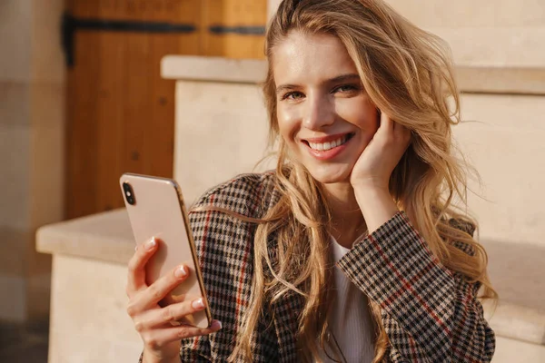 Usmívající Mladá Blondýna Drží Mobilní Telefon Zatímco Sedí Schodech Ulici — Stock fotografie