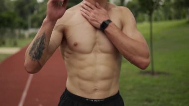 Yakışıklı yarı çıplak bir adam stadyumda yürüyor.