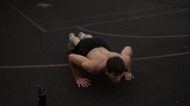 Spor sahasında antrenman yaparken kaslı bir adam yukarı itiyor.