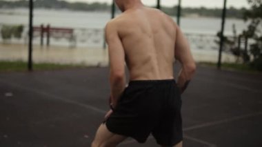 Yarı çıplak bir adam yağmur sırasında spor alanında basketbol oynuyor.