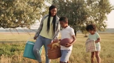 Mutlu bir aile, çayırda bir şeyler taşırken piknik yapacak.