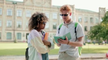 Öğrenci kadın ve erkek güneş gözlüğü takmış kampüsün dışında konuşuyorlar.