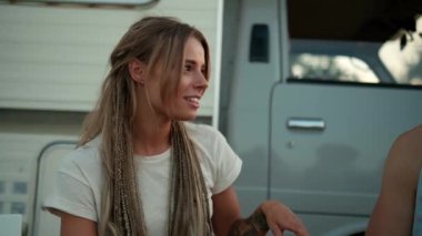 Güzel bir kadın dışarıda karavanın yanındaki piknik sırasında arkadaşlarıyla oturup konuşuyor.