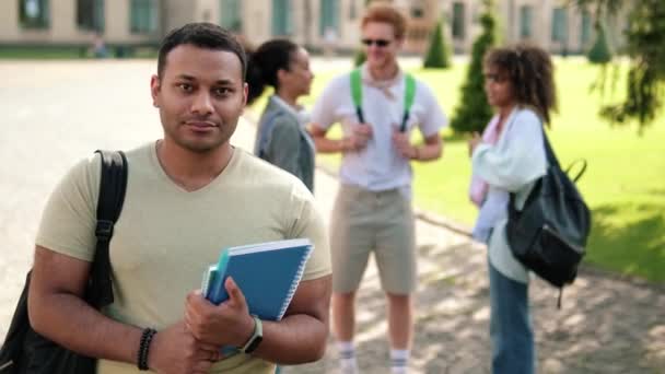 笑顔のアメリカ人学生が外のキャンパスに立っているカメラを見ている — ストック動画
