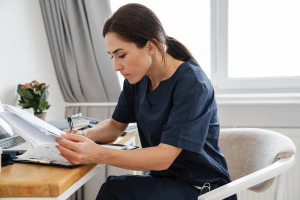 Zaostřená Žena Lékař Pracuje Notebookem Papíry Zatímco Sedí Stolu Doma — Stock fotografie