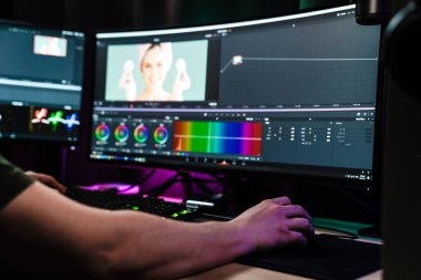 Beyaz bir adamın arka plan görüntüsü büyük bir ekranın önünde oturan video düzenleyicisi kapalı alanda bir video montajı üzerinde çalışıyor.