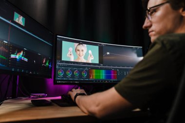 Beyaz bir adamın arka plan görüntüsü büyük bir ekranın önünde oturan video düzenleyicisi kapalı alanda bir video montajı üzerinde çalışıyor.