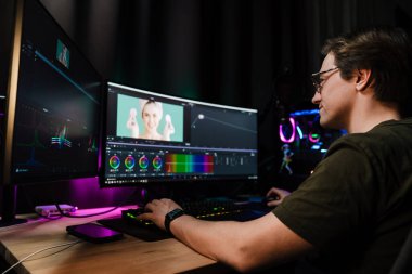 Beyaz bir adamın arka plan görüntüsü büyük bir ekranın önünde oturan video düzenleyicisi kapalı alanda bir video montajı üzerinde çalışıyor.