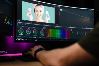 Beyaz bir adamın arka plan görüntüsü büyük bir ekranın önünde oturan video düzenleyicisi kapalı alanda bir video montajı üzerinde çalışıyor.