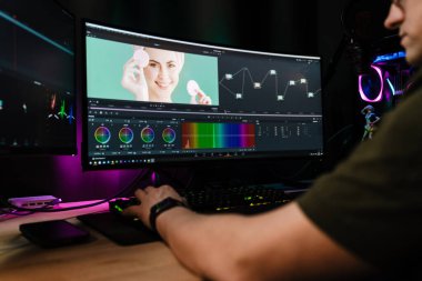 Beyaz bir adamın arka plan görüntüsü büyük bir ekranın önünde oturan video düzenleyicisi kapalı alanda bir video montajı üzerinde çalışıyor.