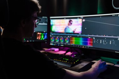 Beyaz bir adamın arka plan görüntüsü büyük bir ekranın önünde oturan video düzenleyicisi kapalı alanda bir video montajı üzerinde çalışıyor.