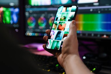 Beyaz bir adamın cep telefonunu kapalı bir masadaki bilgisayar ekranında tutarken.