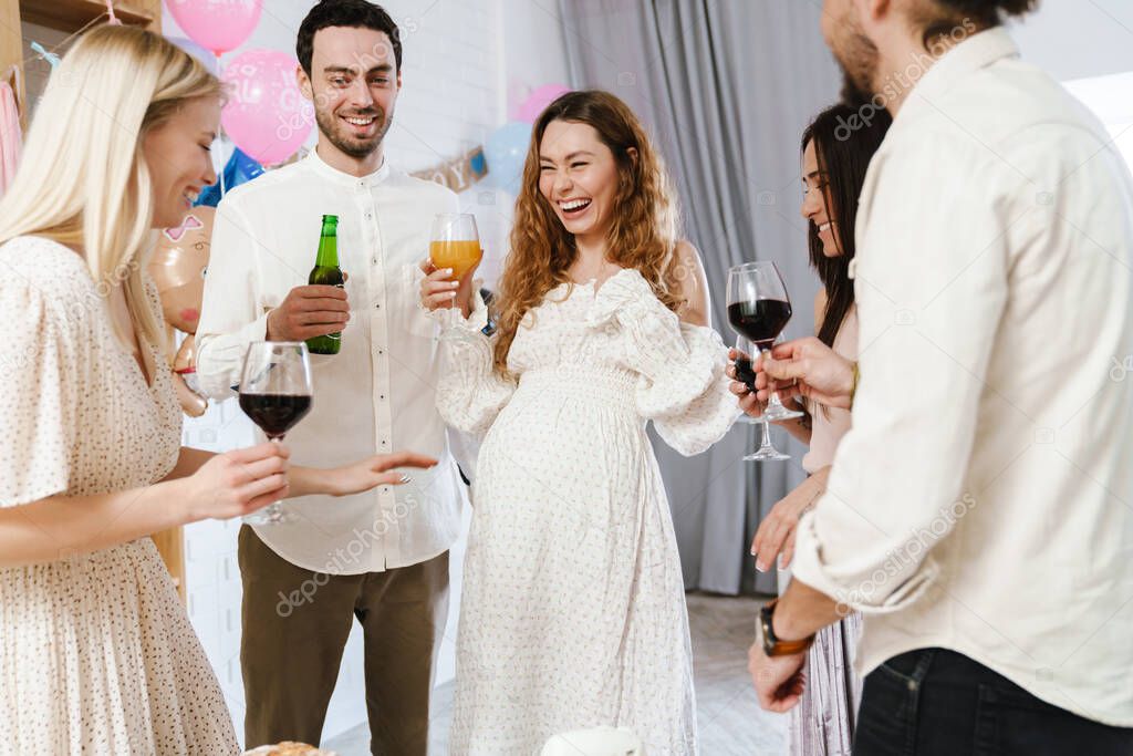 Young happy pregnant woman making fun with her friends during gender reveal party indoors