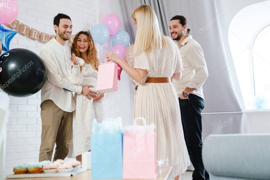 Young happy couple accepting gifts from her friend during gender reveal party indoors