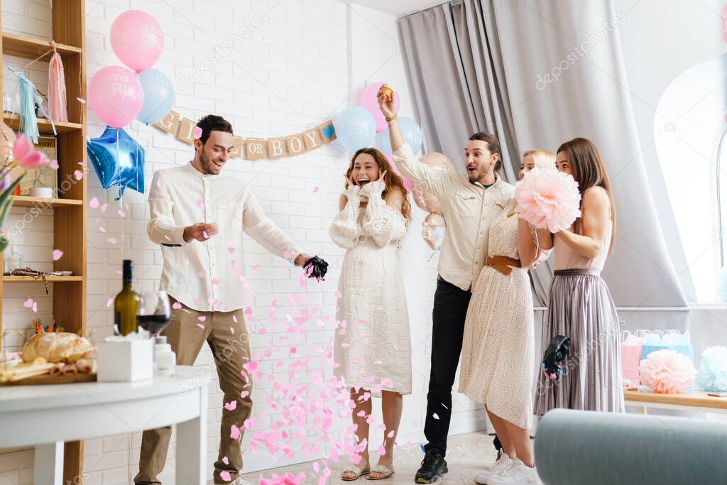 Young excited couple blowing up surprise balloon during gender reveal party indoors