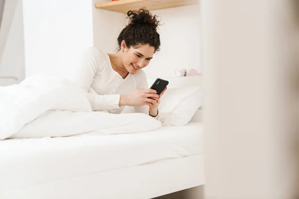 Mujer Sonriente Mirando Teléfono Mientras Está Acostada Cama Pijama Blanco —  Fotos de Stock