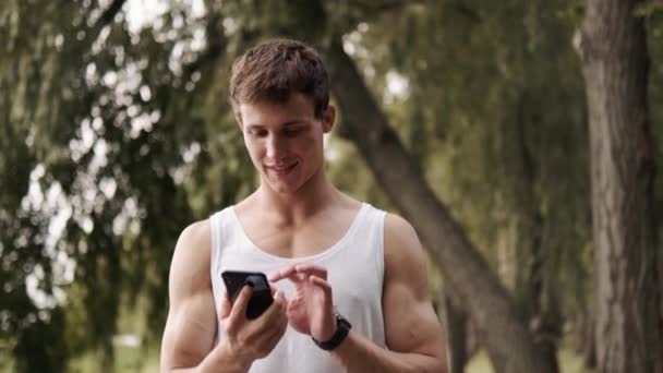 Een Knappe Vent Zet Zijn Mobieltje Uit Het Park Buiten — Stockvideo