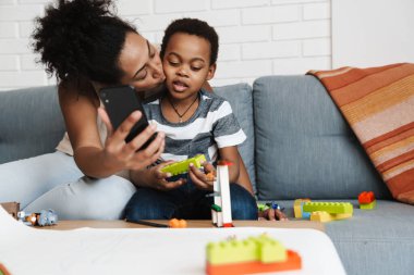 Siyahi, gülümseyen bir kadın cep telefonuyla oğlunu kucaklarken kendi fotoğrafını çekiyor.